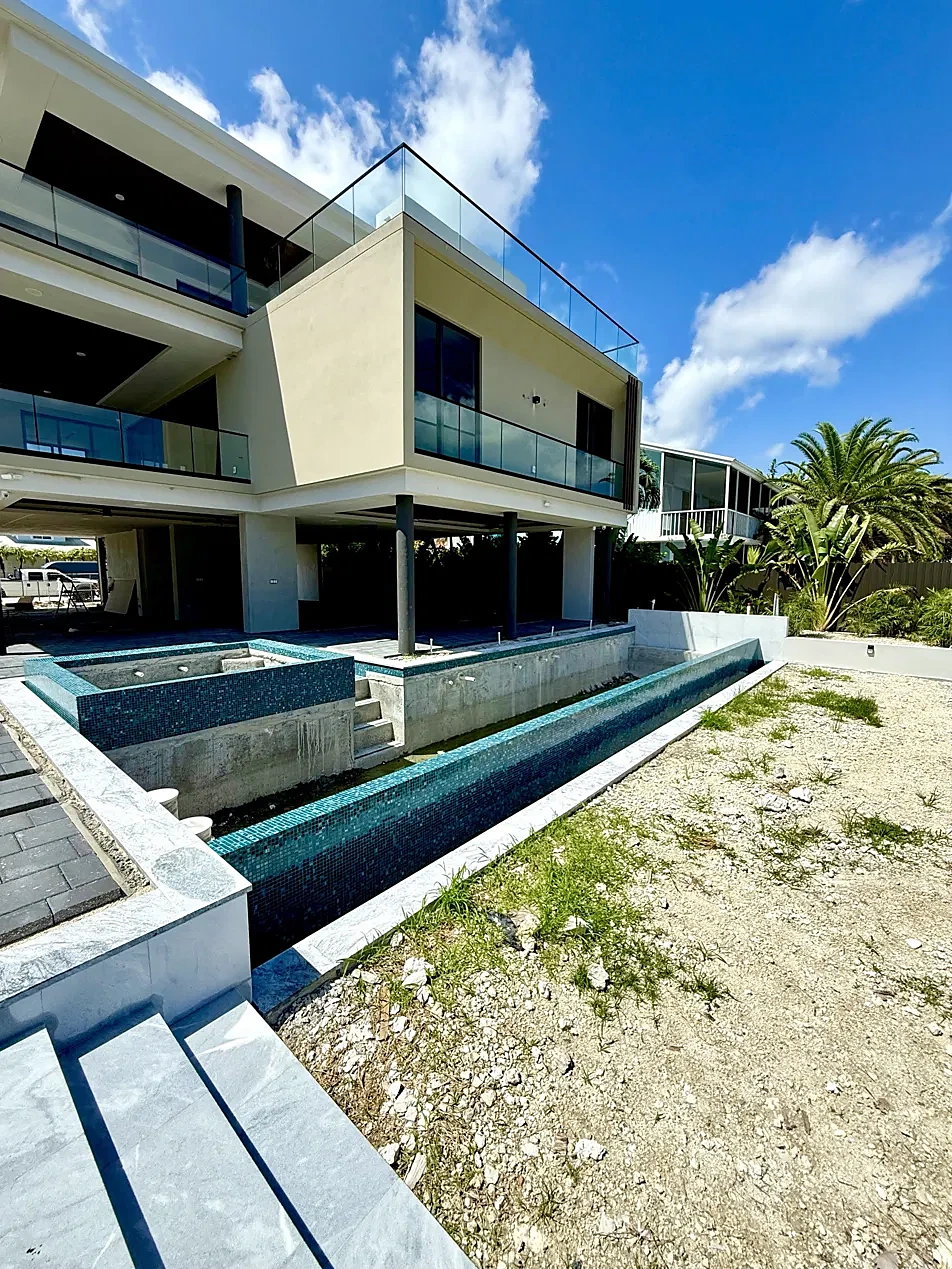 Pool under construction: glass-tile infinity pool and raised spa shell beside a modern home, before decking and landscaping