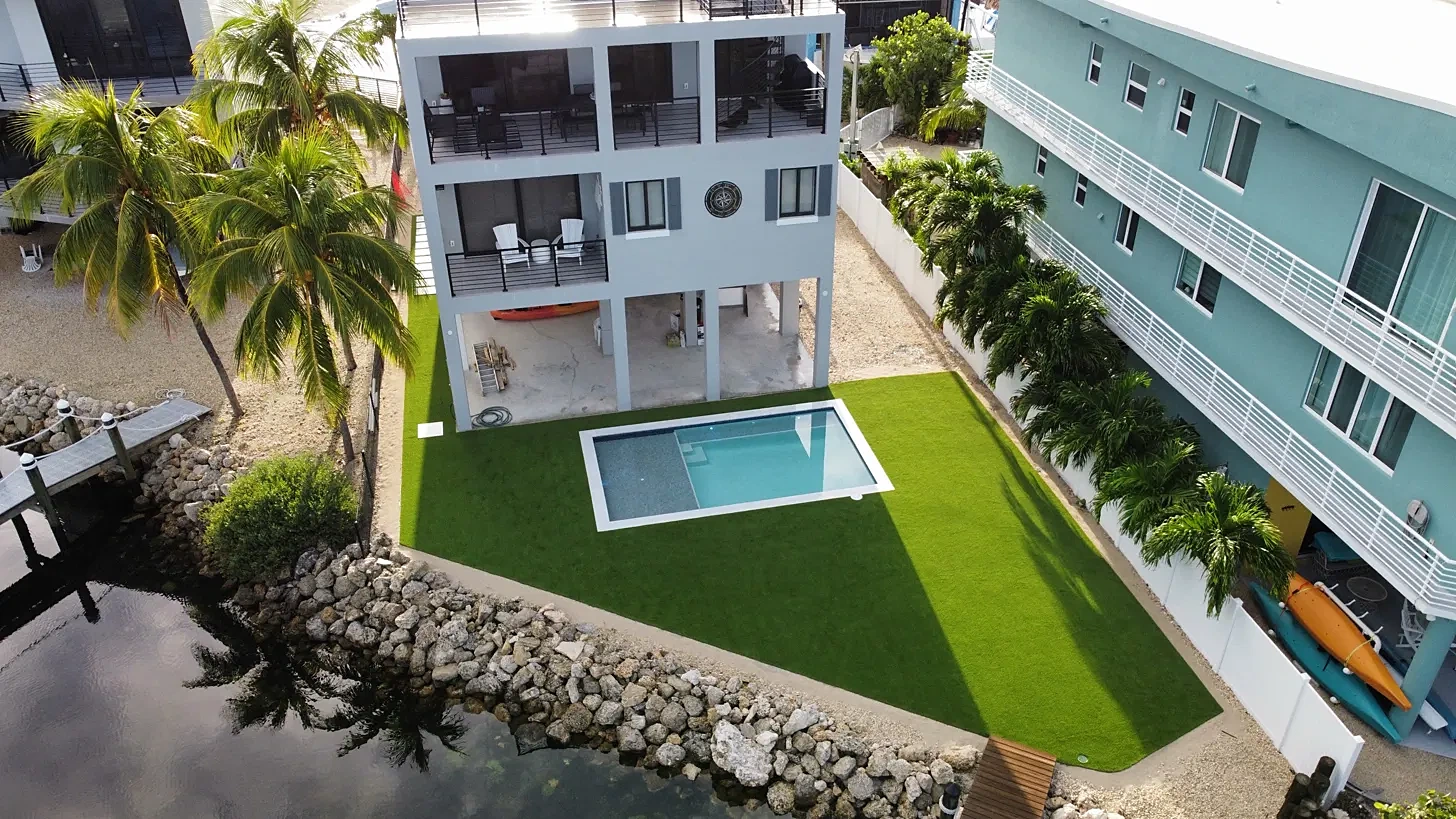 Drone view of a canal-front pool surrounded by artificial turf next to a boat dock in the Florida Keys