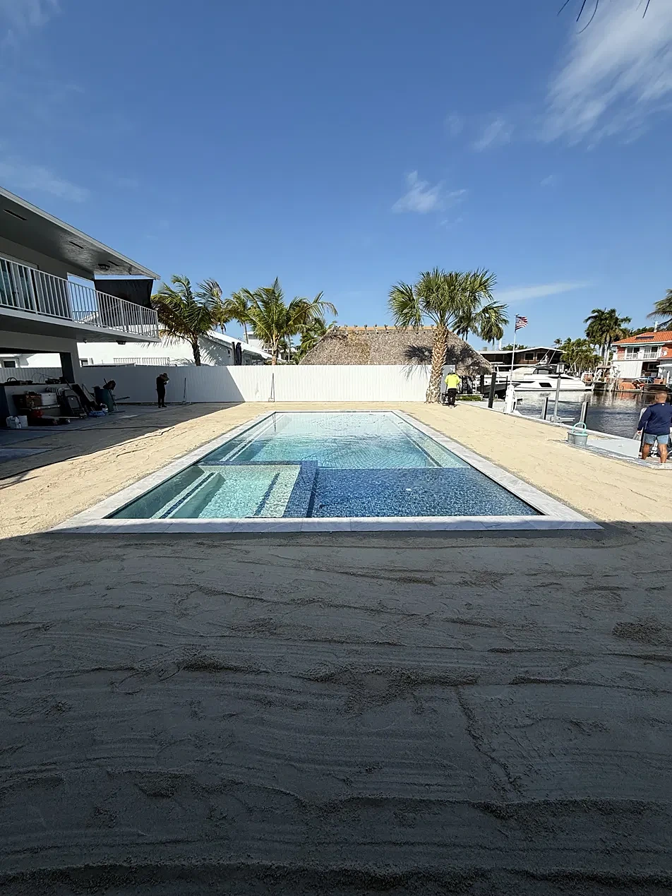 Newly finished canal-front pool with sun shelf and white privacy fence, before decking and landscaping
