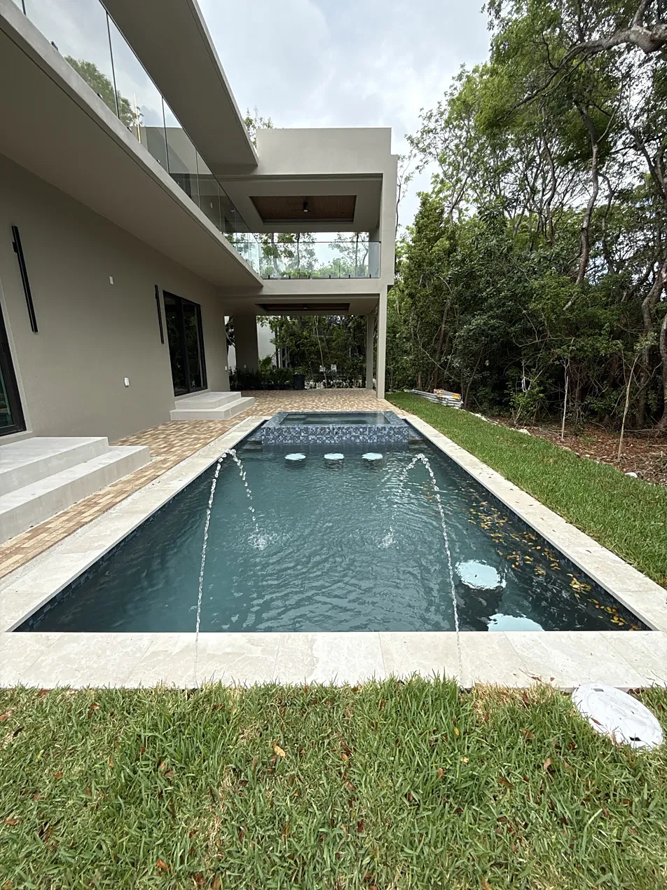 Modern pool with laminar deck jets, spa and paver patio beside a new home
