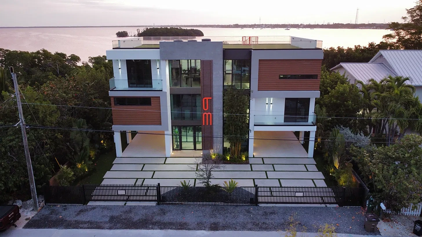 Drone view of a modern bayfront home with a concrete paver driveway and glass balconies