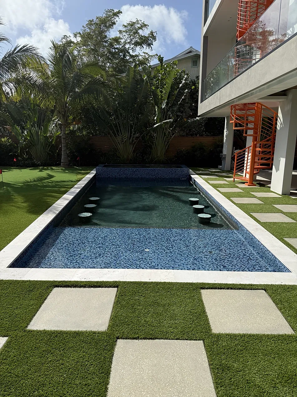 Pool with in-water bar stools beside a modern home with an orange spiral staircase