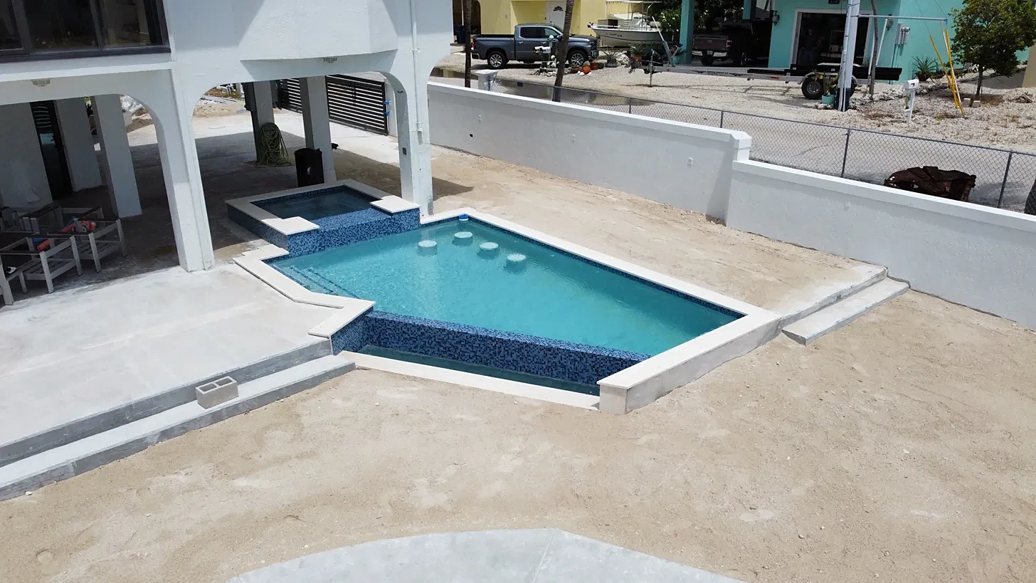 New pool with raised spa and swim-up seats before landscaping, with white CBS privacy walls