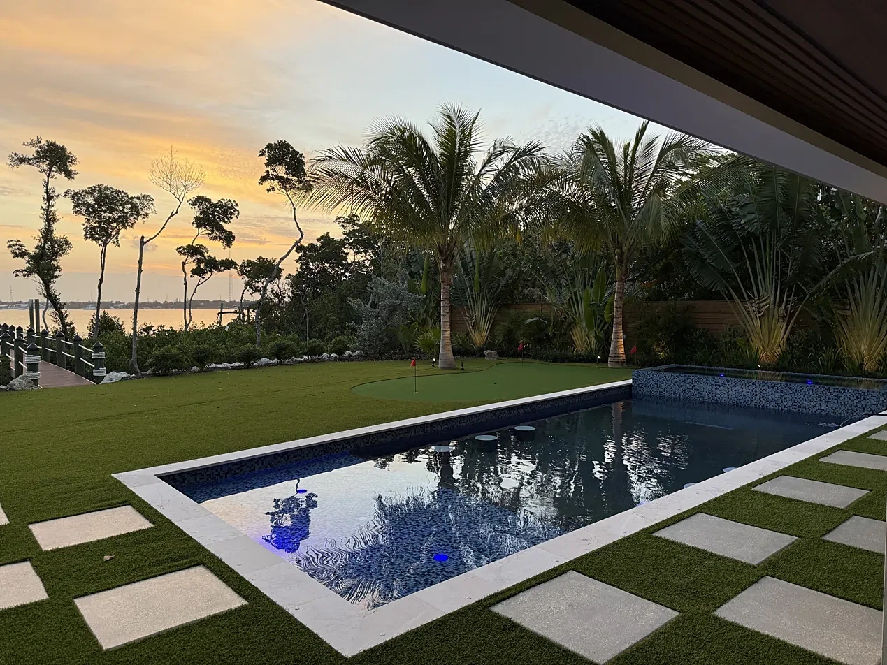 Pool reflecting palm trees at sunset with turf and concrete stepping pavers