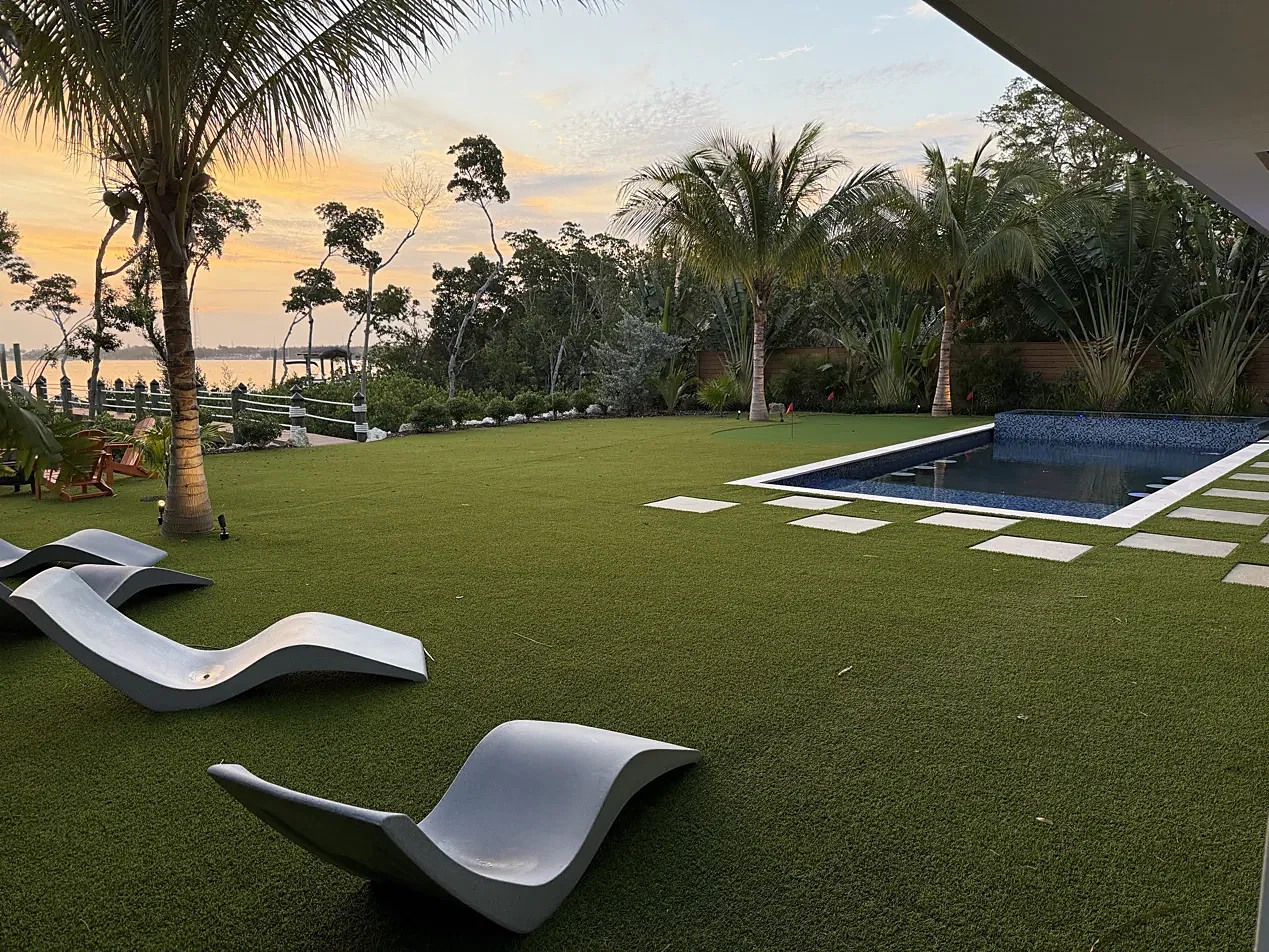 Artificial turf lawn with lounge chairs, pool and putting green at sunset on the water