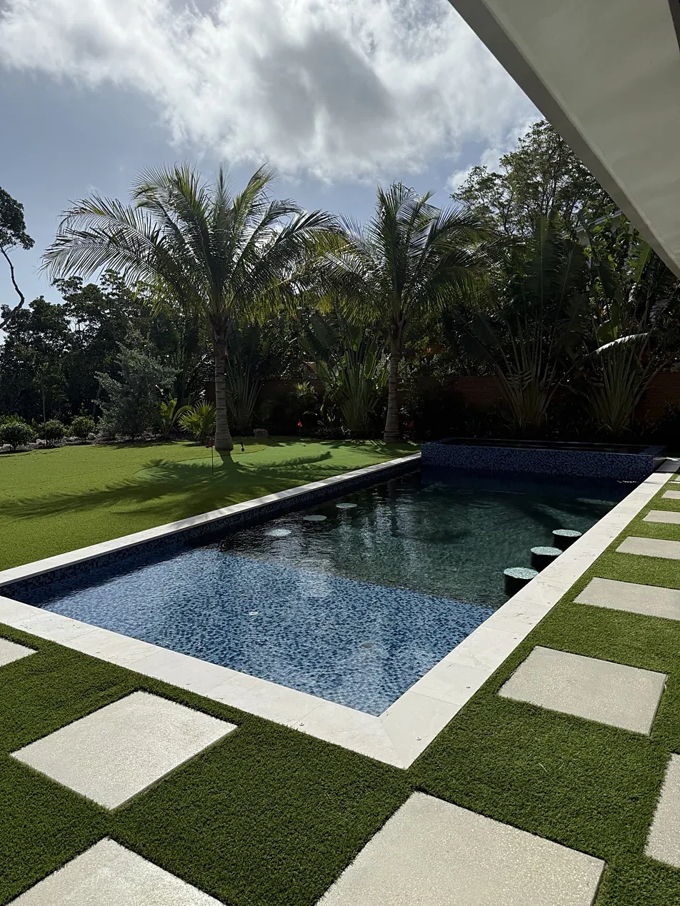 Pool with blue glass tile, marble coping and stepping pavers set in artificial turf