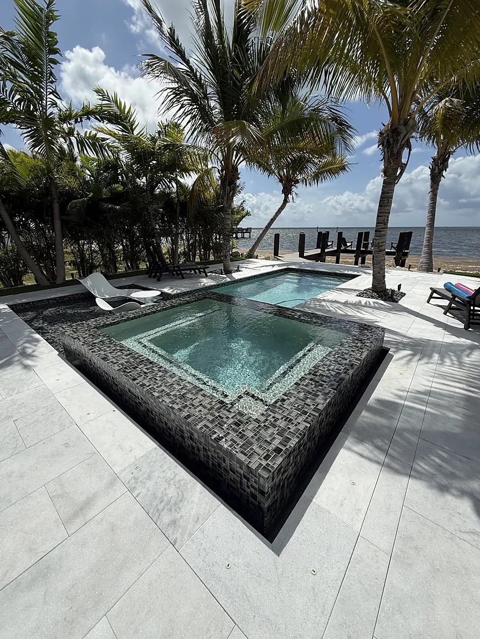 Raised glass-tile spa and pool with marble deck, palms and private dock on the bay